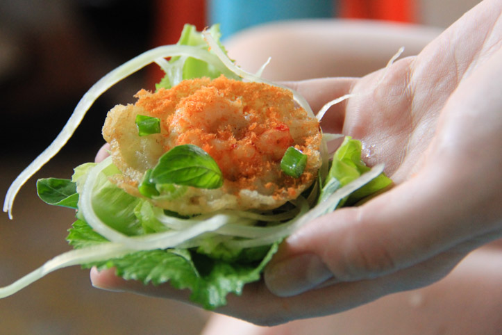 Banh Khot or mini shrimp sizzling pancakes with herbs and in a lettuce leaf before being wrapped